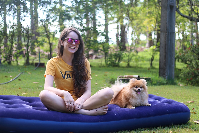 Pomeranian is laying next to his owner on their blue inflatable bed